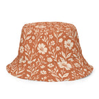 Wendbarer Bucket Hat Canyon Bloom mit Wildblumen-Silhouette in Cremeweiß auf Terrakotta-Grund.